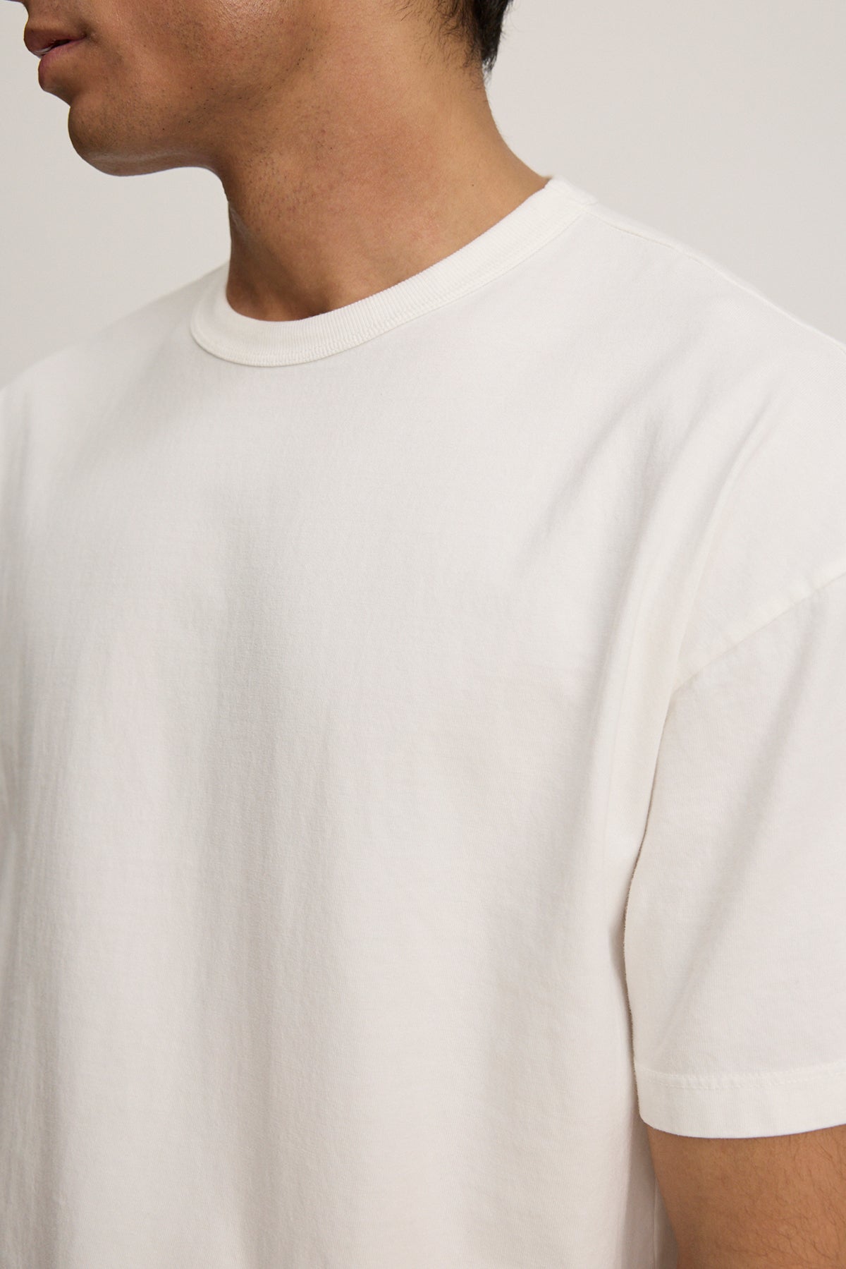   A person models a relaxed fit BRYAN TEE in white, crafted from structured Pima cotton by Velvet by Graham & Spencer, against a neutral backdrop to highlight its everyday versatility. 