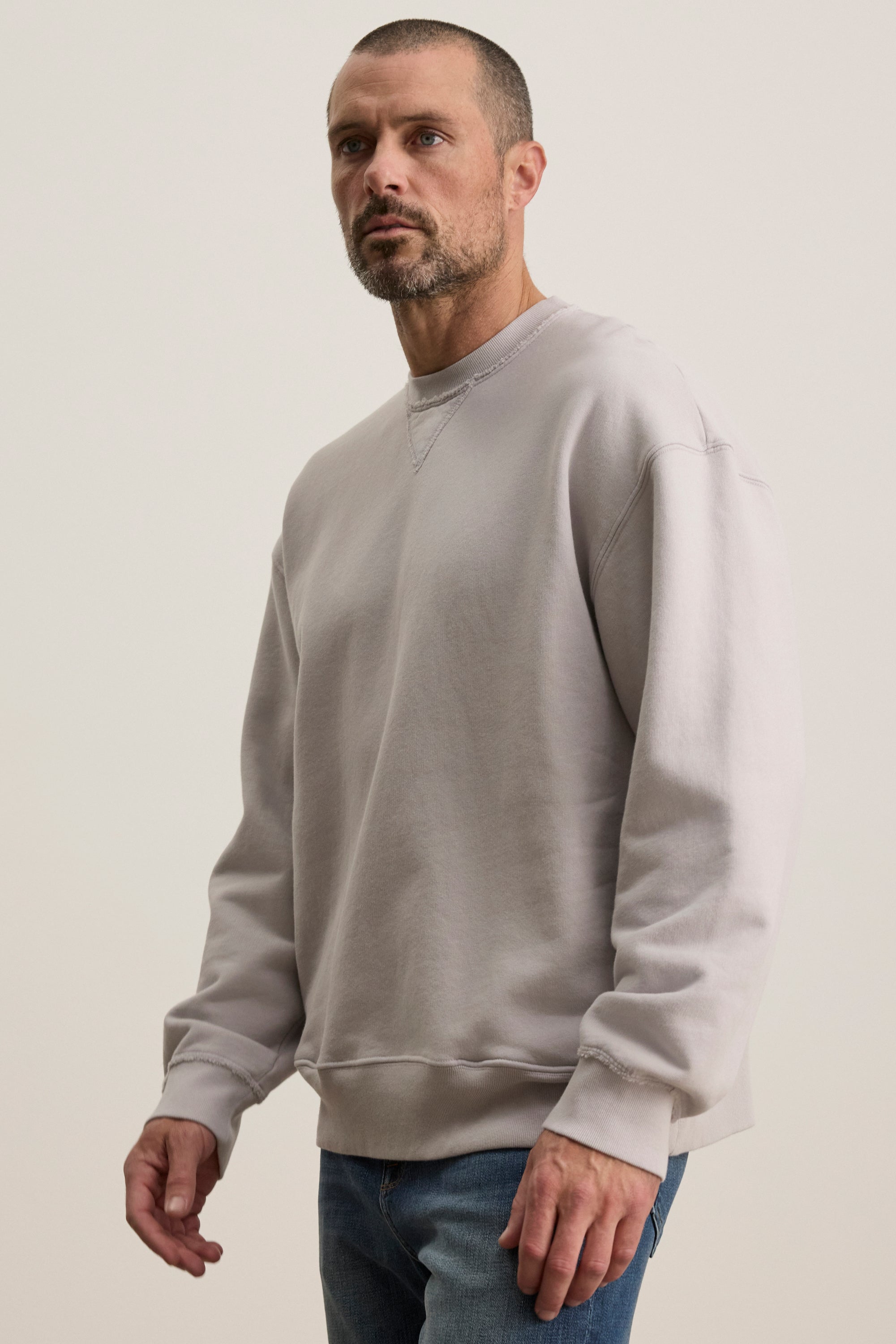   A person wearing the Velvet by Graham & Spencer FORREST SWEATSHIRT in a relaxed fit, made of gray cotton fleece, and blue jeans stands against a plain background, looking to the side. 