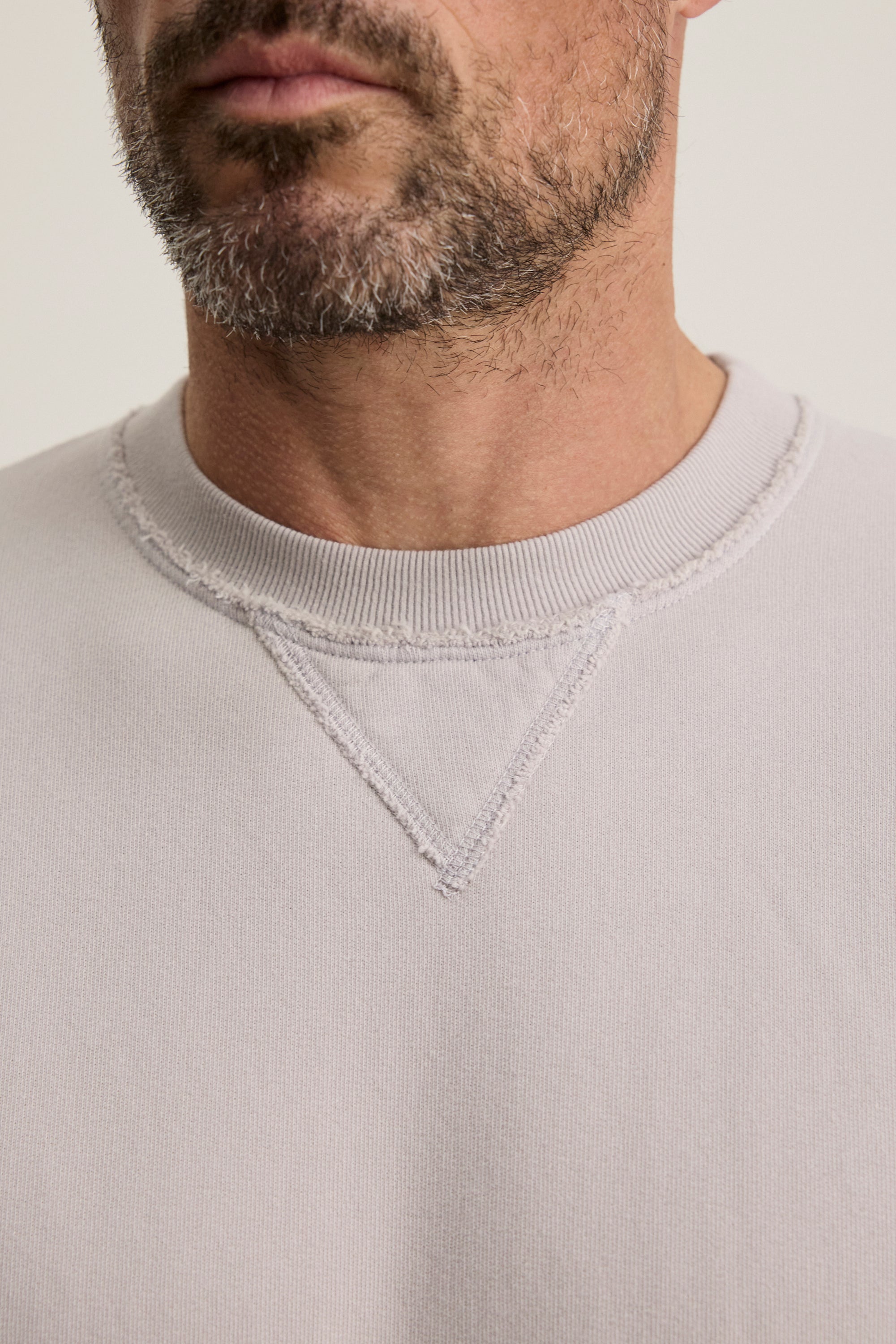   A person with facial hair wears the Velvet by Graham & Spencer FORREST SWEATSHIRT, a relaxed fit made from soft cotton fleece, featuring a raw hem and V-stitch detail below the collar. 