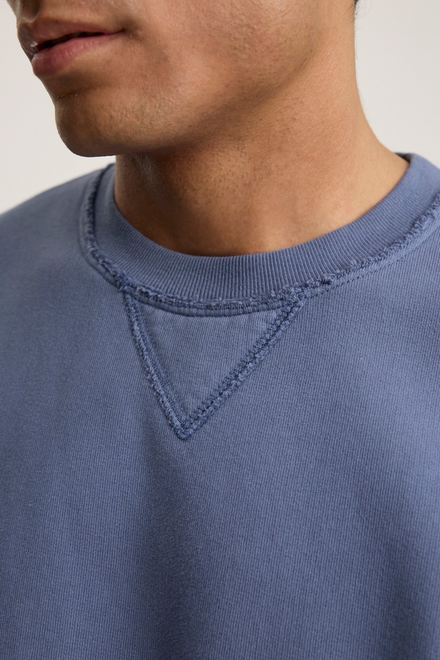 Close-up of a person wearing the Velvet by Graham & Spencer FORREST SWEATSHIRT, a blue cotton fleece with visible stitching on the collar and featuring a relaxed fit.-38500141105345