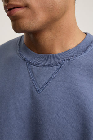 Close-up of a person wearing the Velvet by Graham & Spencer FORREST SWEATSHIRT, a blue cotton fleece with visible stitching on the collar and featuring a relaxed fit.