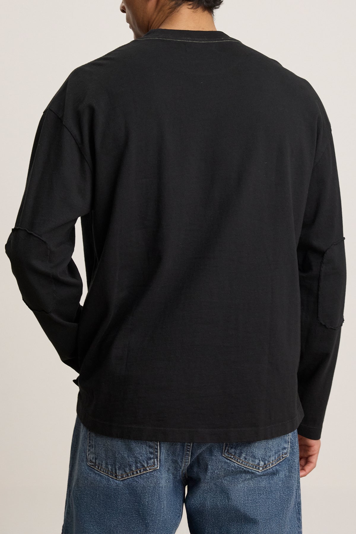   Individual dressed in the Velvet by Graham & Spencer SLATER TEE, a black long-sleeve shirt crafted from structured pima cotton, along with relaxed-fit blue jeans, pictured from behind. 