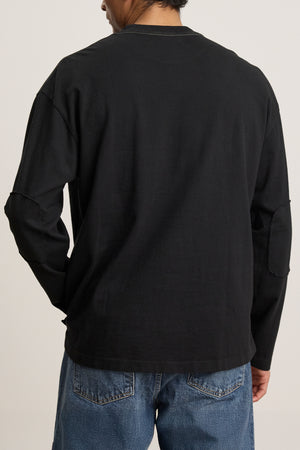 Individual dressed in the Velvet by Graham & Spencer SLATER TEE, a black long-sleeve shirt crafted from structured pima cotton, along with relaxed-fit blue jeans, pictured from behind.