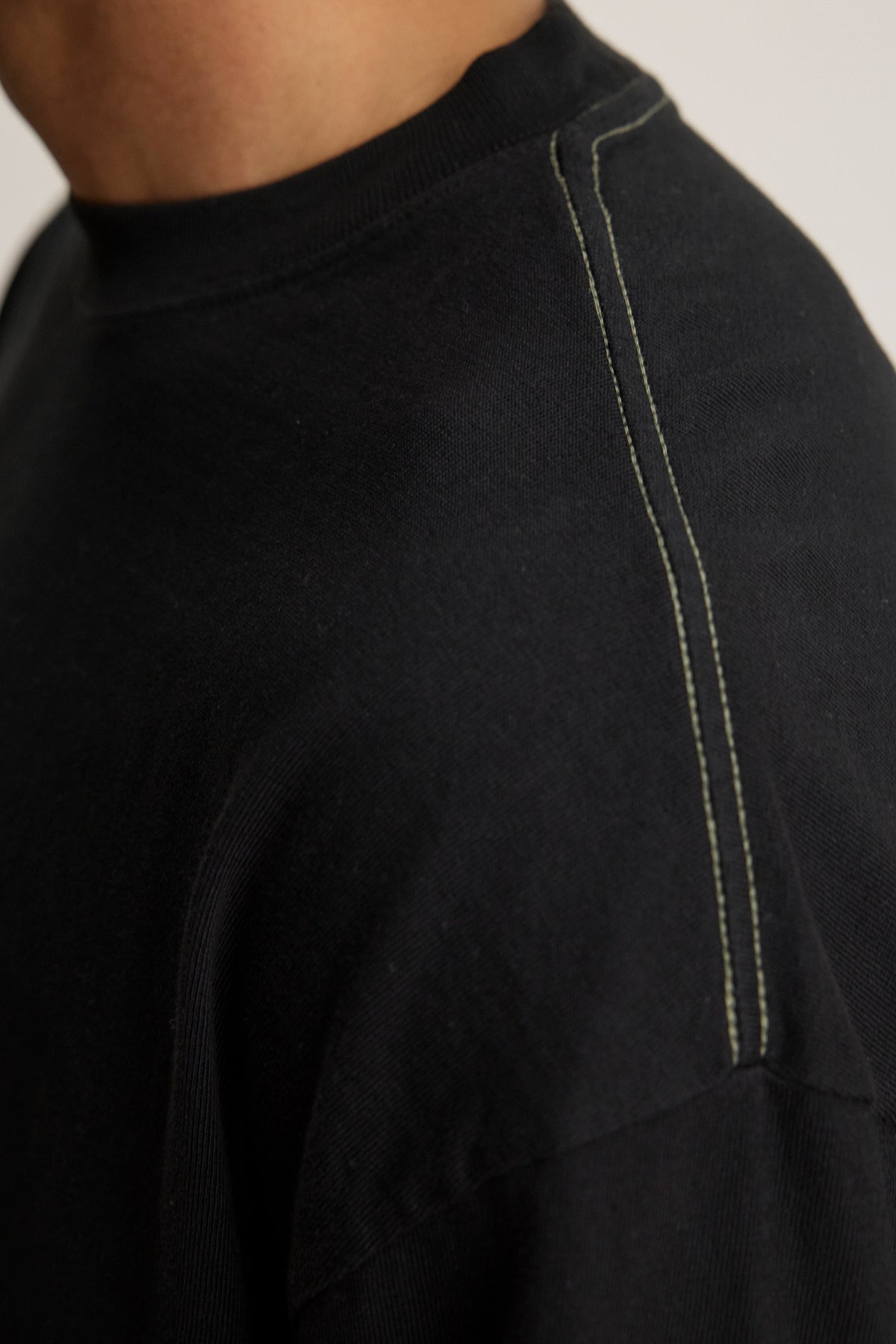 Close-up of someone in the SLATER TEE by Velvet by Graham & Spencer, a black pima cotton jersey shirt with visible white stitching on the shoulder seam. This relaxed fit piece adds versatility to any wardrobe.-38500088611009