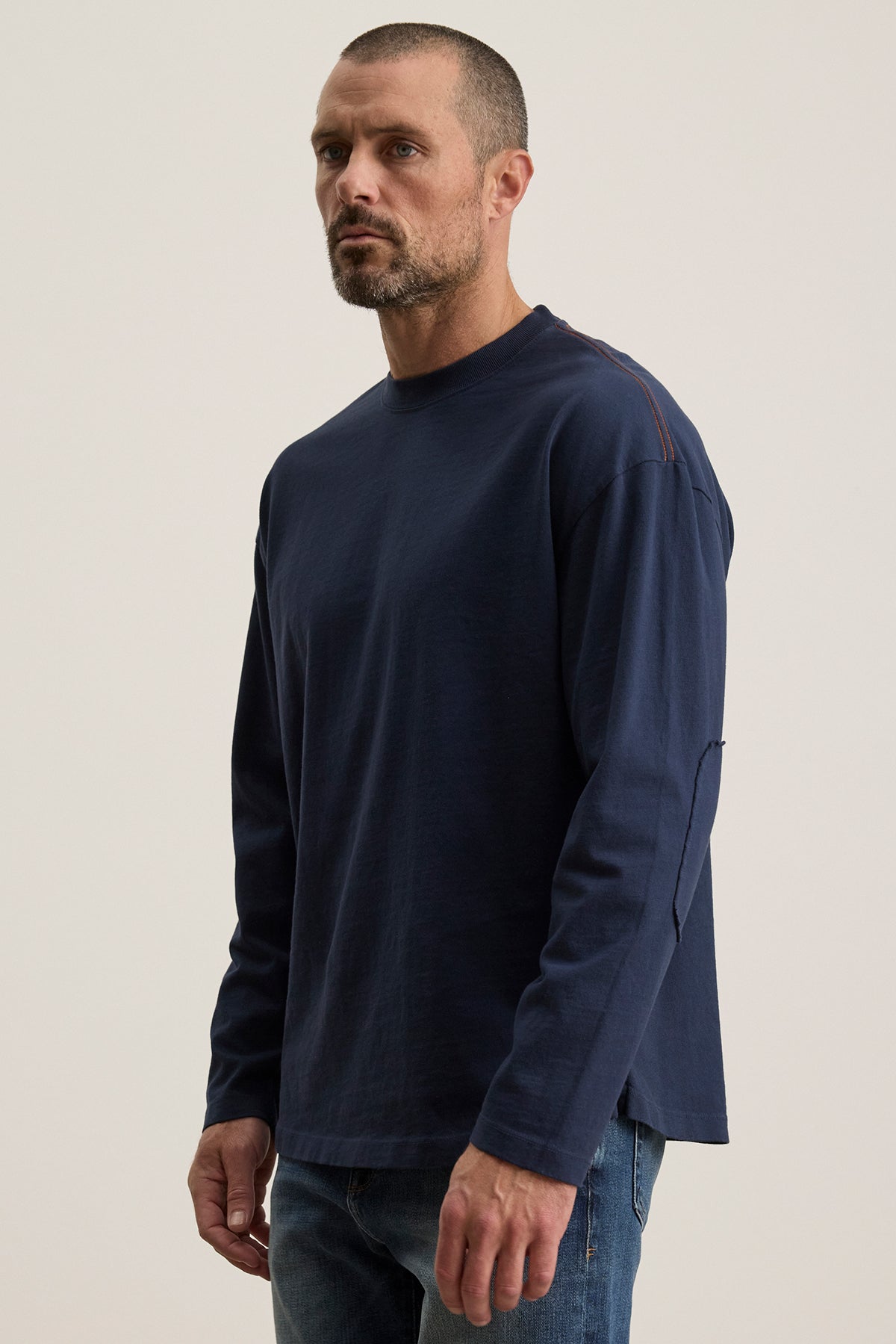   A person with short hair and a beard is wearing a Velvet by Graham & Spencer SLATER TEE in navy and jeans, posed against a plain background. 