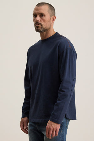 A person with short hair and a beard is wearing a Velvet by Graham & Spencer SLATER TEE in navy and jeans, posed against a plain background.