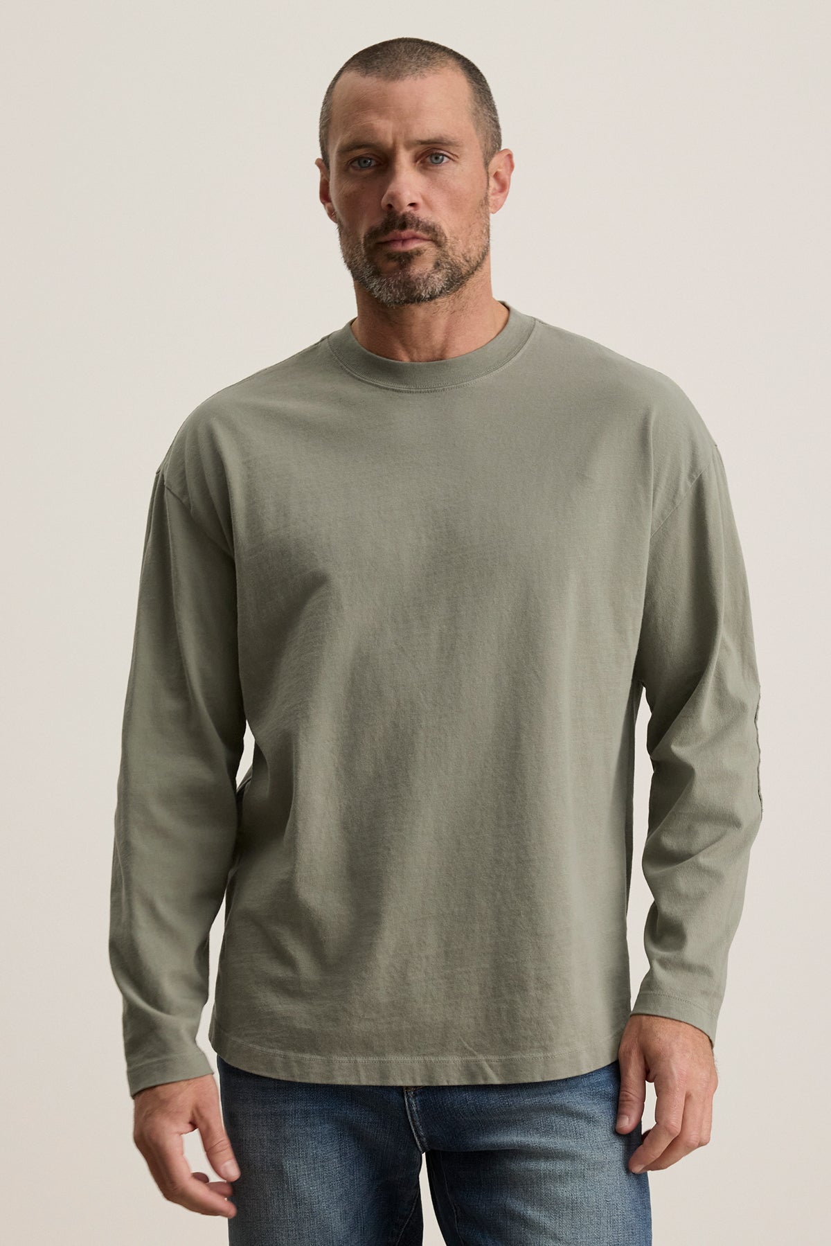 A bearded man with short hair wears the Velvet by Graham & Spencer SLATER TEE in light green, a relaxed-fit long-sleeve shirt made from structured Pima cotton, paired with blue jeans against a plain backdrop.-38500109582529