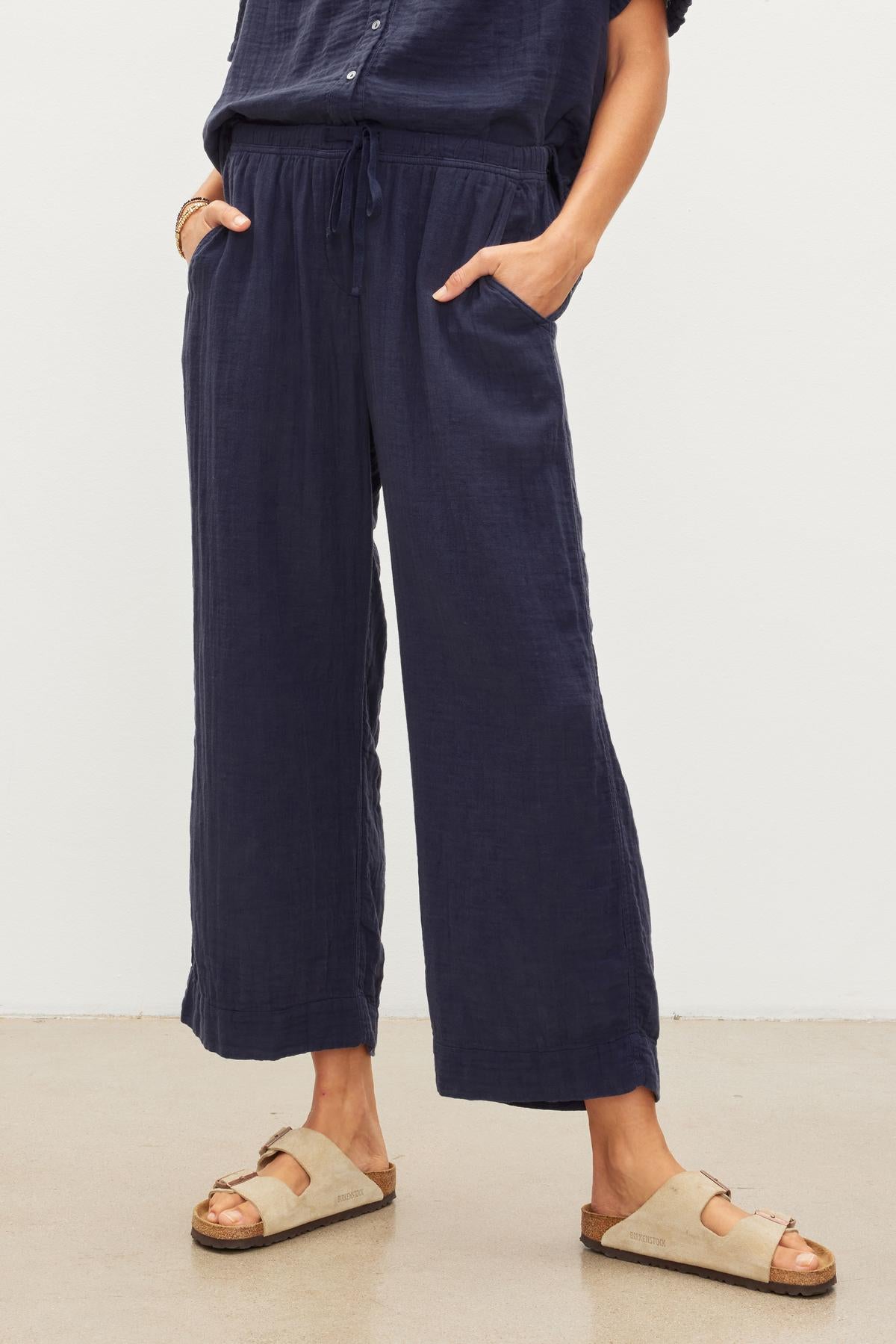   Woman standing in navy blue FRANNY COTTON GAUZE drawstring pants from Velvet by Graham & Spencer with relaxed leg and beige sandals. 