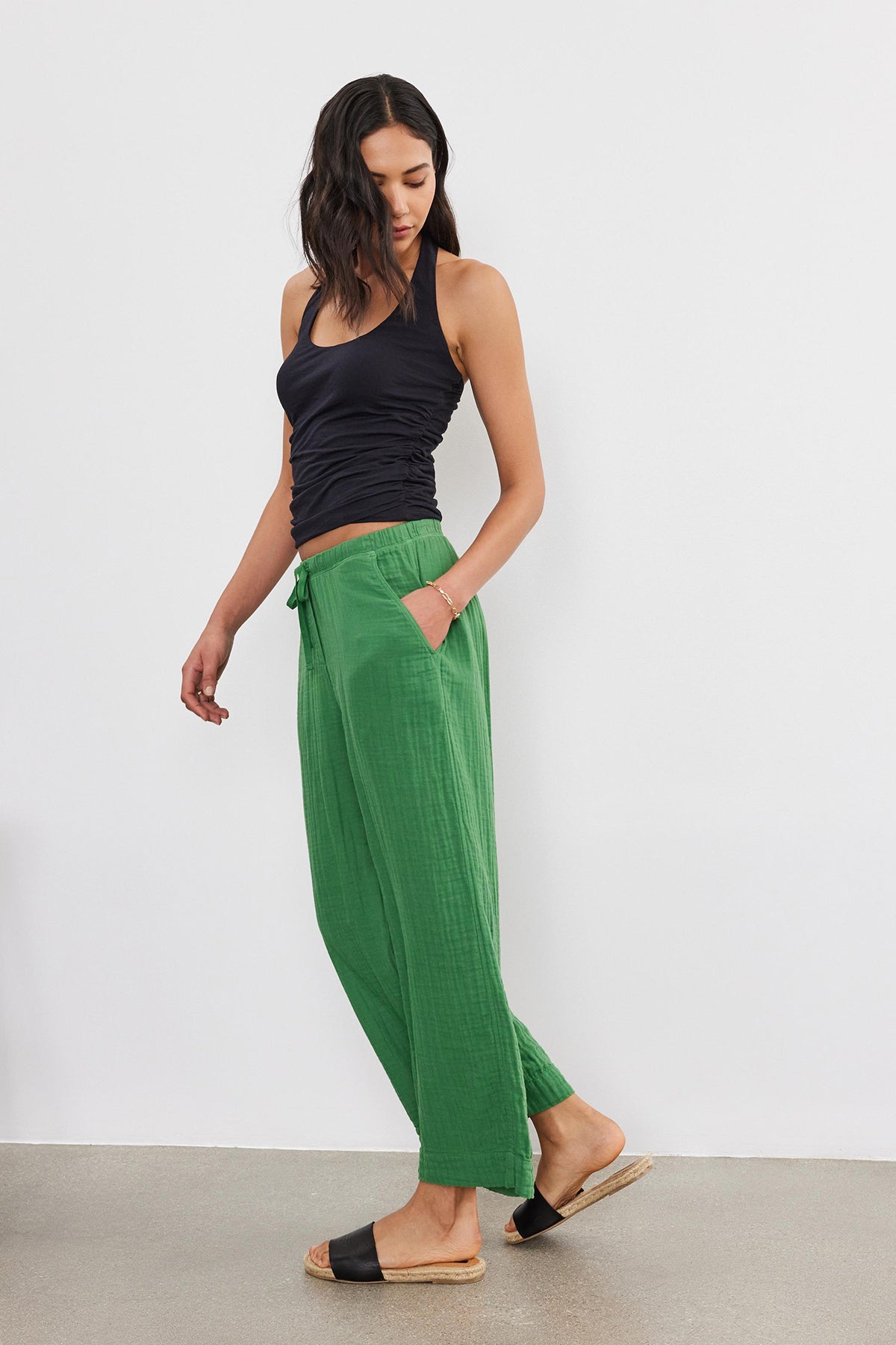   A woman in a black tank top and Velvet by Graham & Spencer Franny Cotton Gauze Pants with relaxed legs stands against a plain background, her hand resting on her hip. 