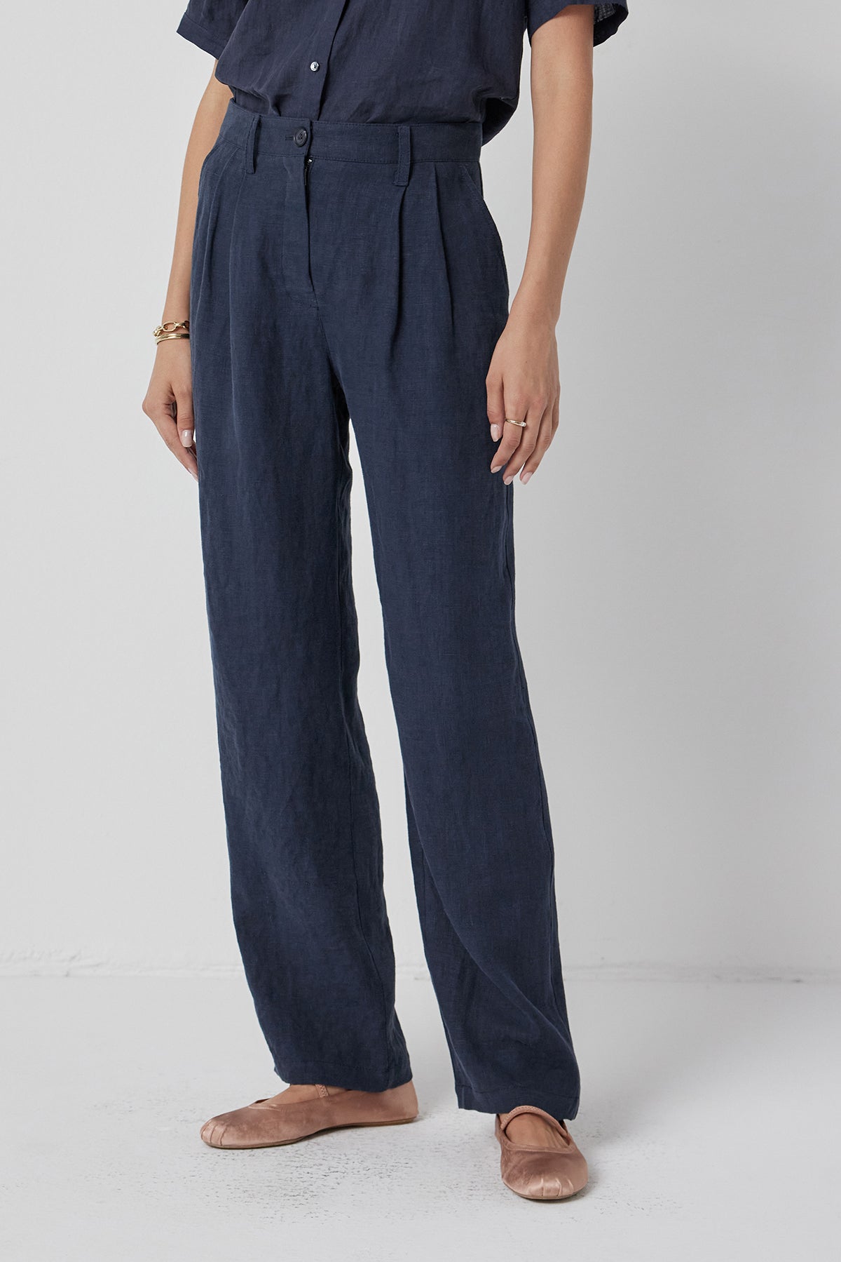   A person wearing Velvet by Jenny Graham's POMONA PANT, a heavy-weight linen, dark blue jumpsuit paired with brown shoes, standing against a white background. 