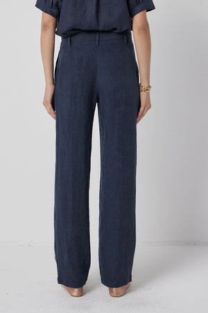 A person standing in Velvet by Jenny Graham's POMONA PANT trousers and a matching top with their hands partially tucked into pockets.