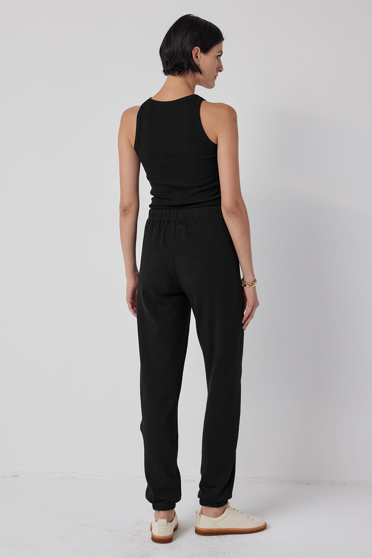   Viewed against a gray background, a person wears the WESTLAKE SWEATPANT by Velvet by Jenny Graham—a stylish pair of joggers made from organic cotton fleece with an elastic drawstring waist—and a black tank top. 