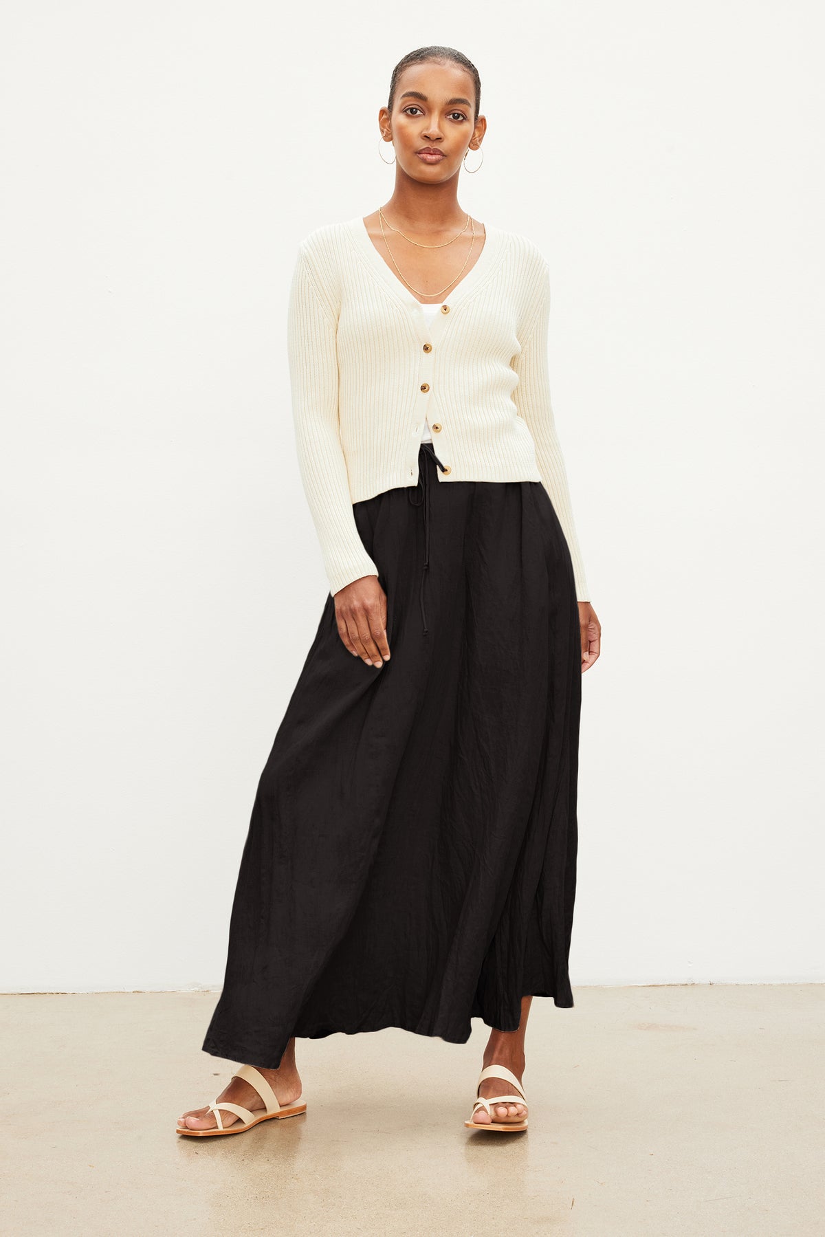   A person stands against a white background wearing a cream sweater, Velvet by Graham & Spencer BAILEY LINEN MAXI SKIRT with an elastic drawstring waist, and sandals. 