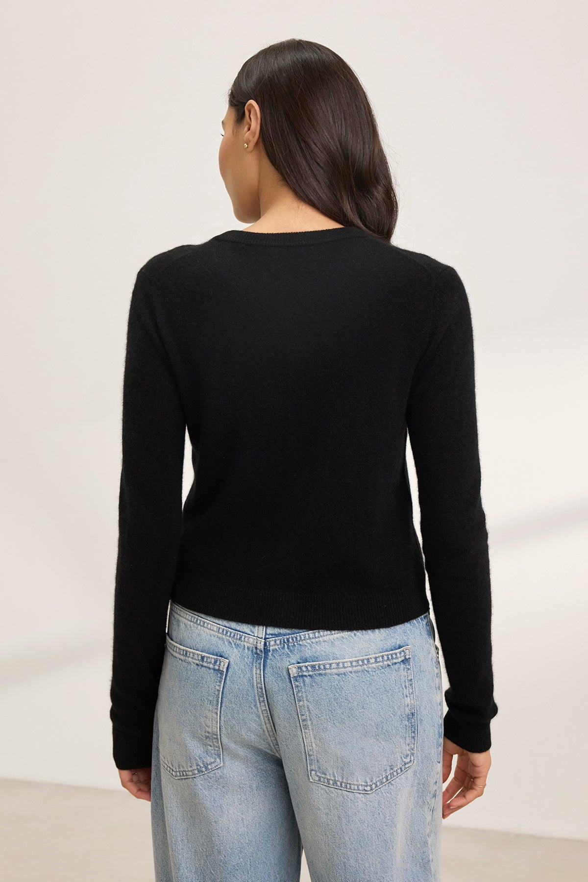   Individual with long dark hair in a CHRICHET CASHMERE CARDIGAN from Velvet by Graham & Spencer and light blue jeans, facing away. 