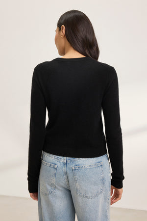 Individual with long dark hair in a CHRICHET CASHMERE CARDIGAN from Velvet by Graham & Spencer and light blue jeans, facing away.