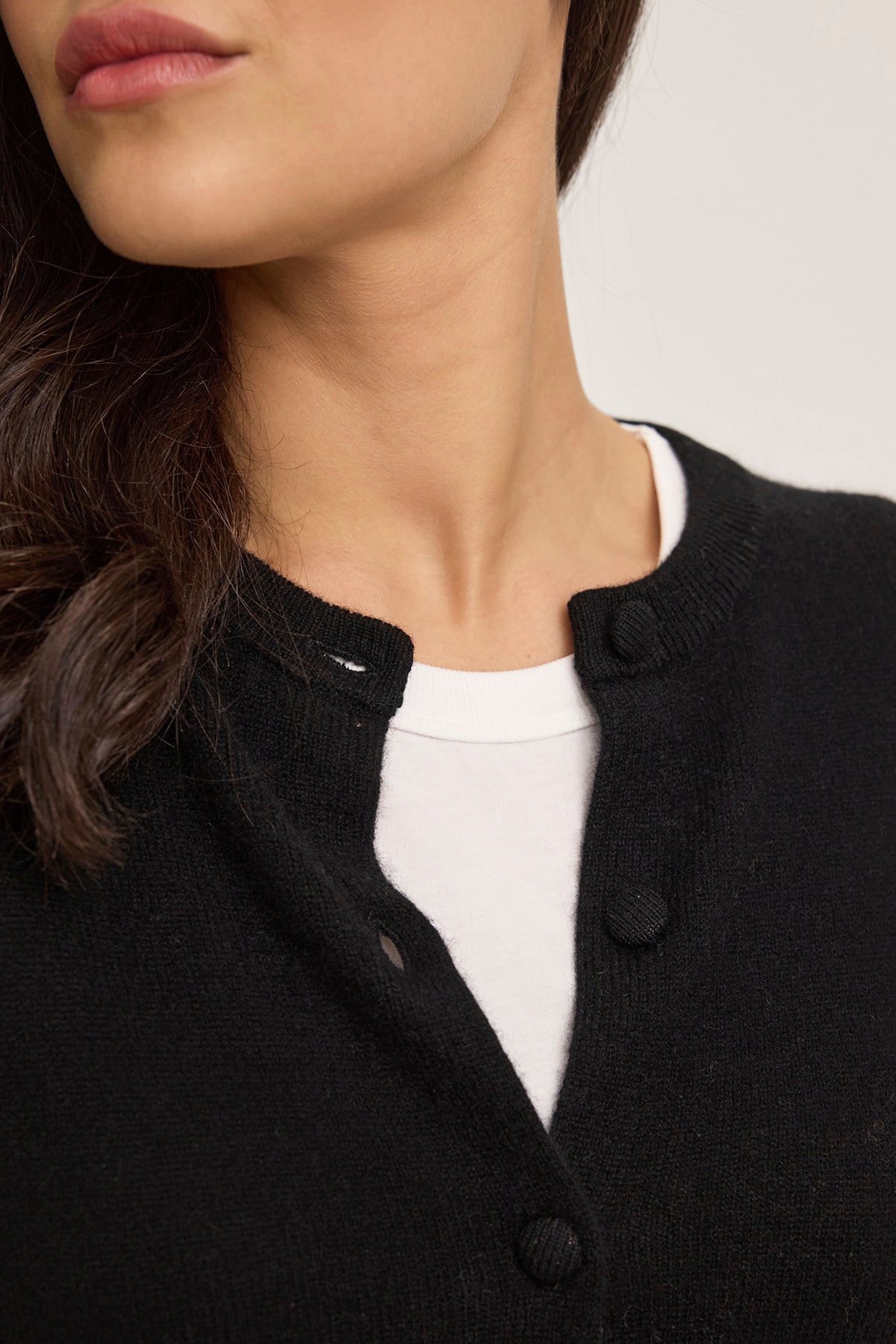   Close-up of a person wearing the CHRICHET CASHMERE CARDIGAN by Velvet by Graham & Spencer over a white shirt, featuring a round neckline with buttons. The person's face is partially visible. 