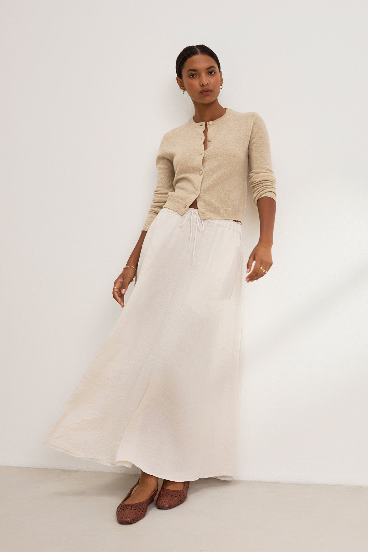   A person models the luxurious CHRICHET CASHMERE CARDIGAN by Velvet by Graham & Spencer, complemented by a beige maxi skirt and brown shoes against a plain white background, effortlessly highlighting this versatile layer. 