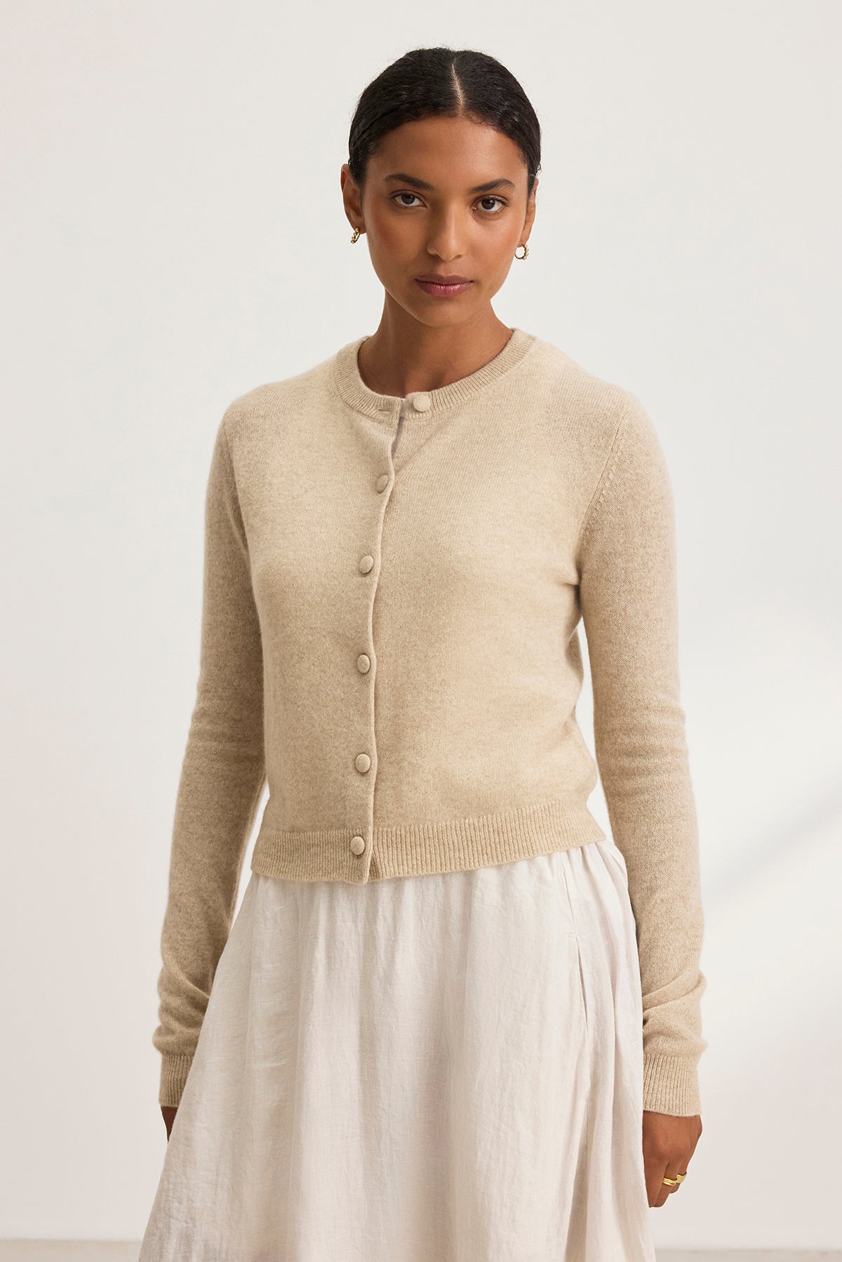   Someone wearing the CHRICHET CASHMERE CARDIGAN by Velvet by Graham & Spencer and a white skirt stands against a plain background. 