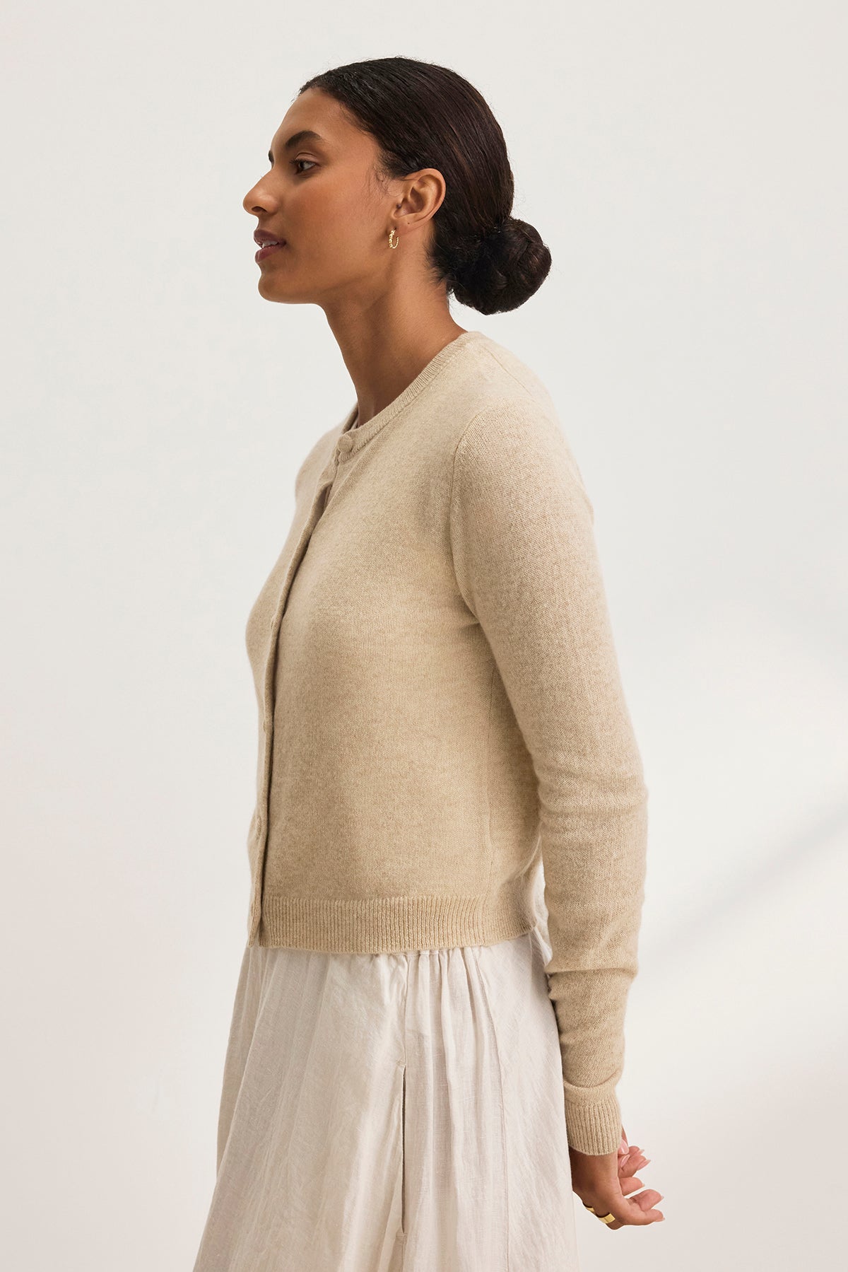   A woman models the CHRICHET CASHMERE CARDIGAN by Velvet by Graham & Spencer with a white skirt set against a light backdrop. 