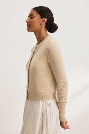 A woman models the CHRICHET CASHMERE CARDIGAN by Velvet by Graham & Spencer with a white skirt set against a light backdrop.