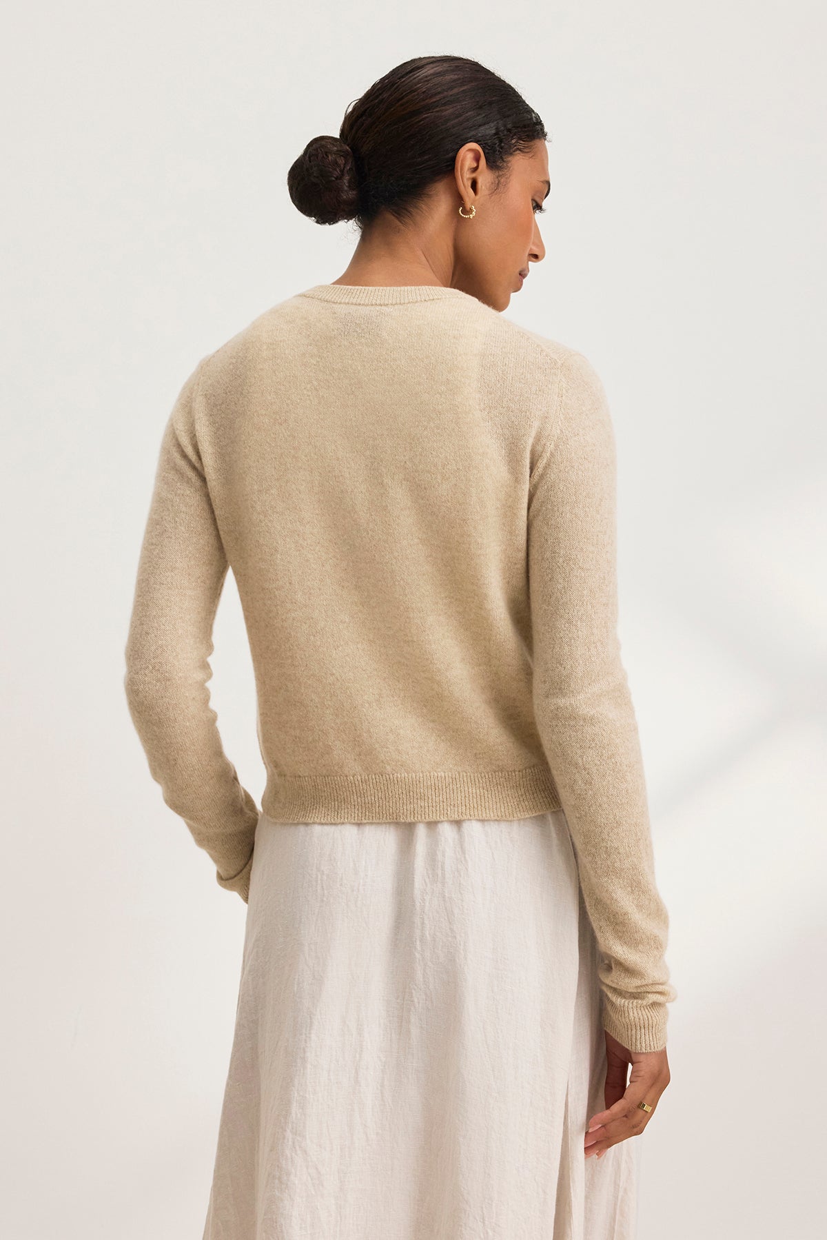   Person with dark hair in a bun, wearing the CHRICHET CASHMERE CARDIGAN by Velvet by Graham & Spencer and a white skirt, facing away. 