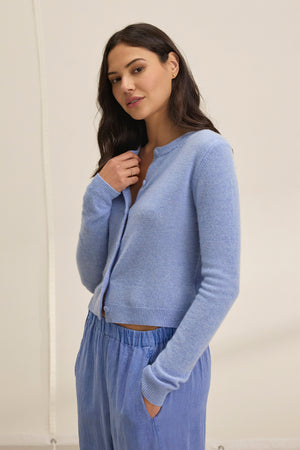 A person in a CHRICHET CASHMERE CARDIGAN by Velvet by Graham & Spencer, paired with blue pants, stands against a neutral background, looking slightly to the side.