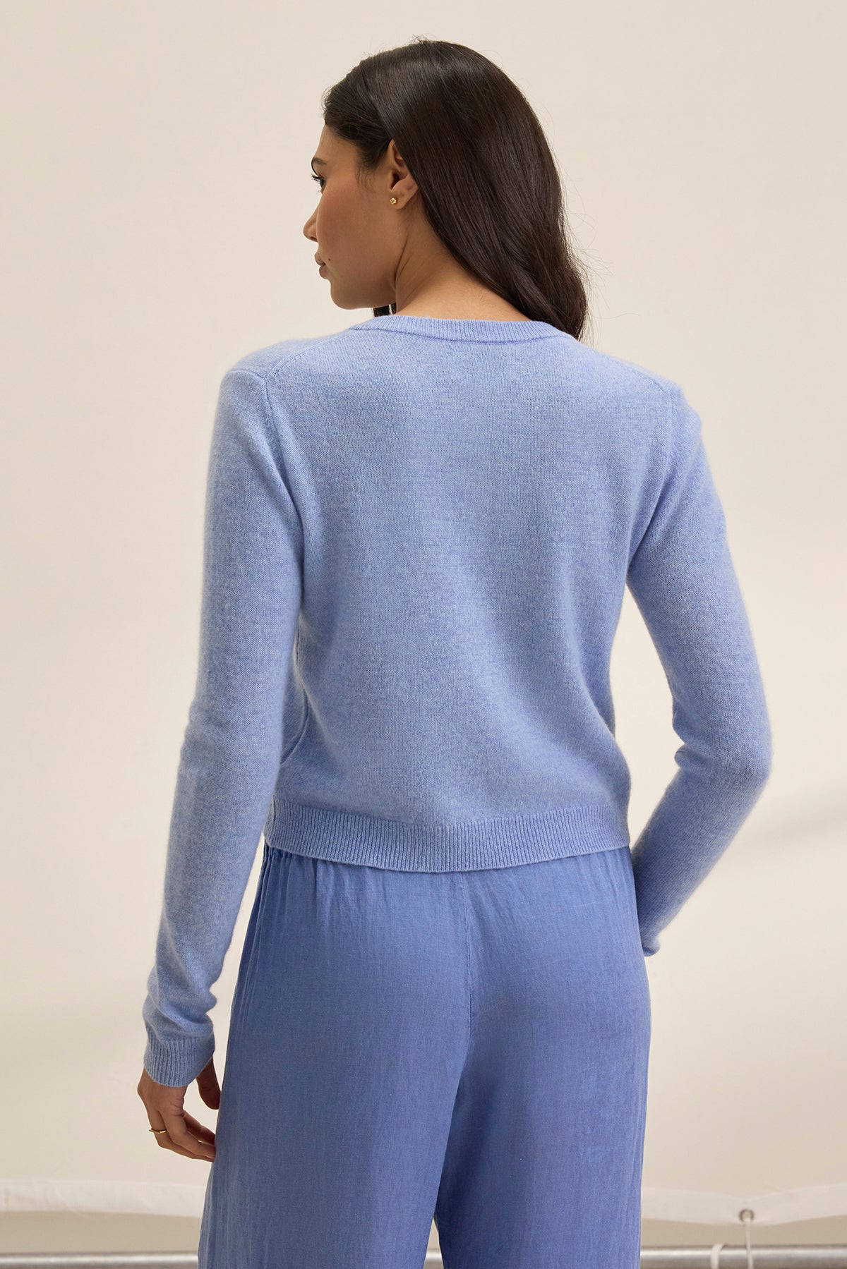   Individual with long hair wearing a Velvet by Graham & Spencer CHRICHET Cashmere Cardigan in light blue, facing away. 