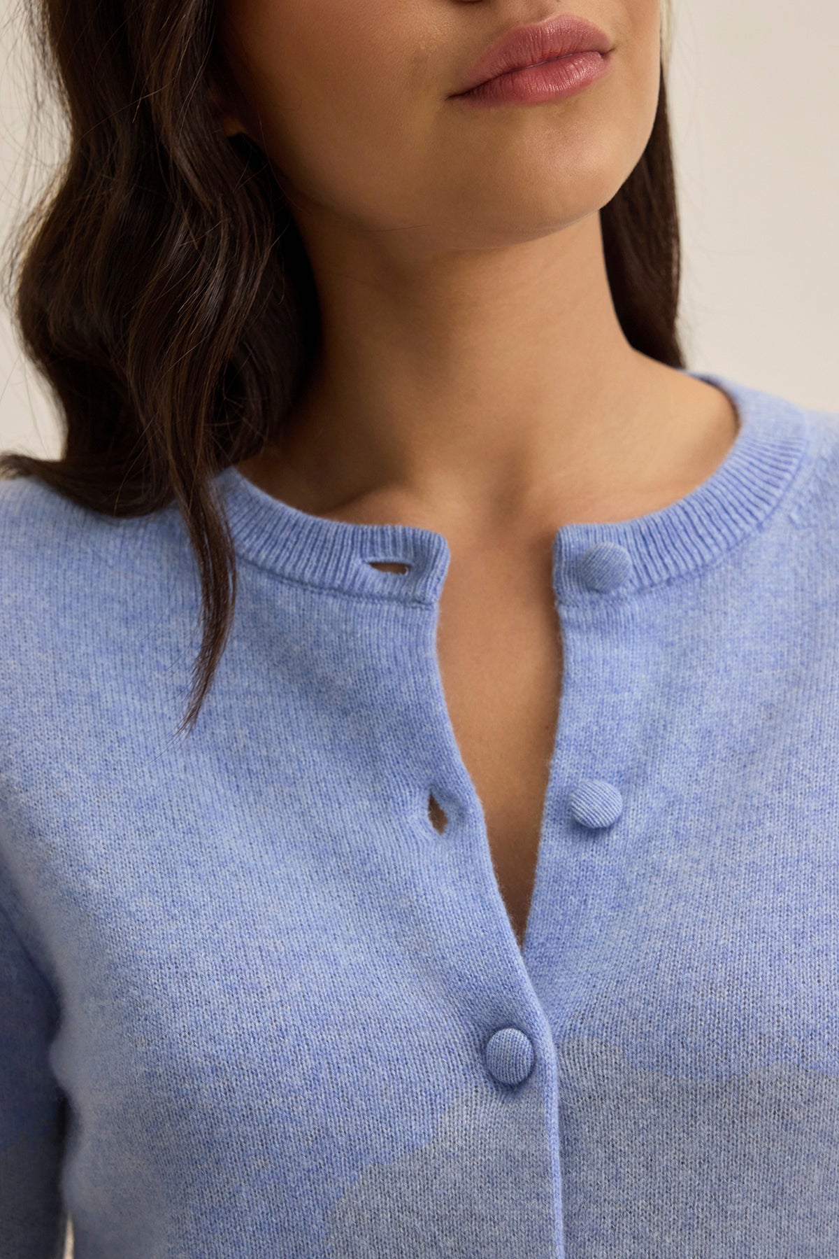   A woman wears a CHRICHET CASHMERE CARDIGAN by Velvet by Graham & Spencer in light blue with the top button undone. Her hair is dark and wavy. 