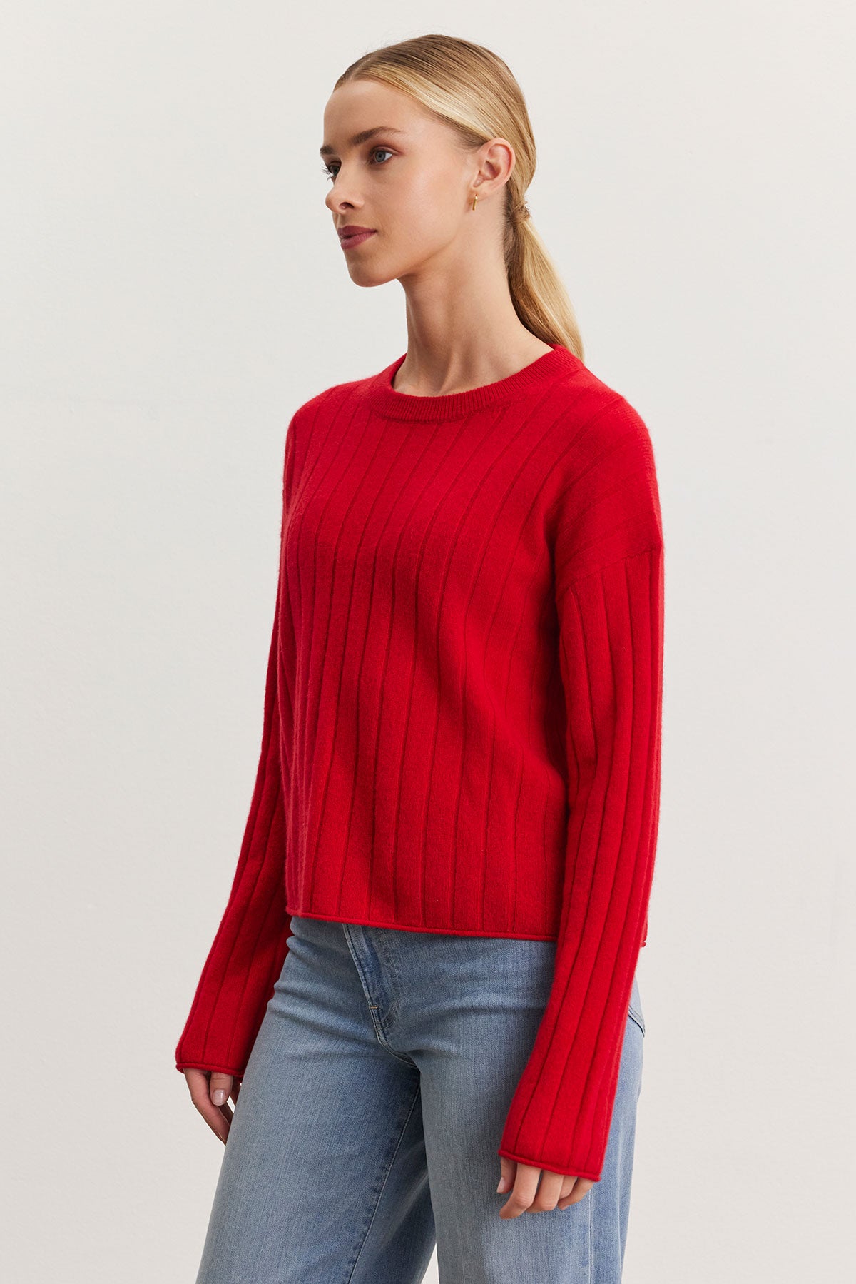 Individual dressed in a red MONICA CASHMERE SWEATER from Velvet by Graham & Spencer and blue jeans, posing against a plain backdrop.-38301411606721