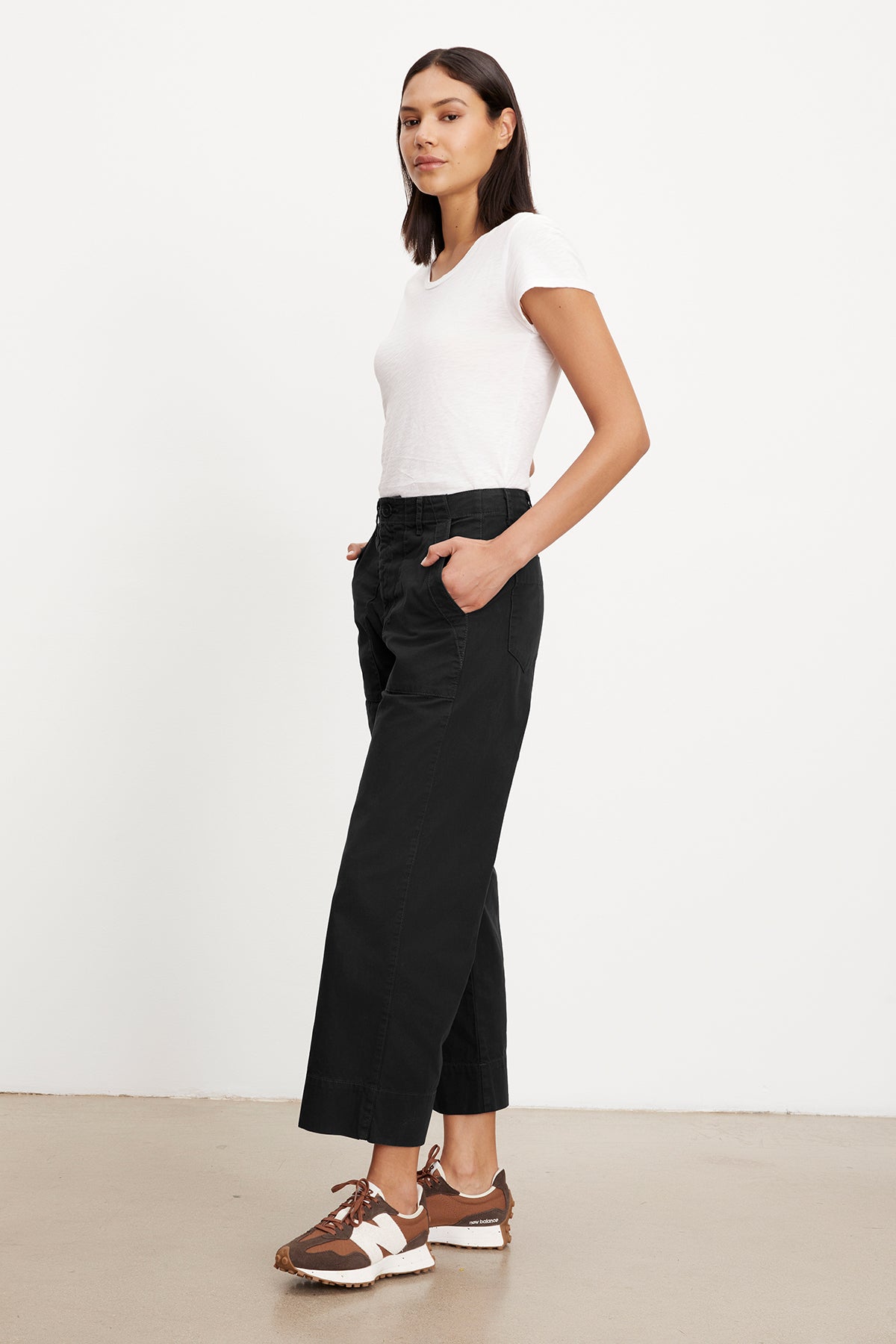 A person stands with hands in pockets, wearing a slim top and Velvet by Graham & Spencer MYA COTTON CANVAS PANT alongside brown sneakers, against a plain white background.-36409563316417