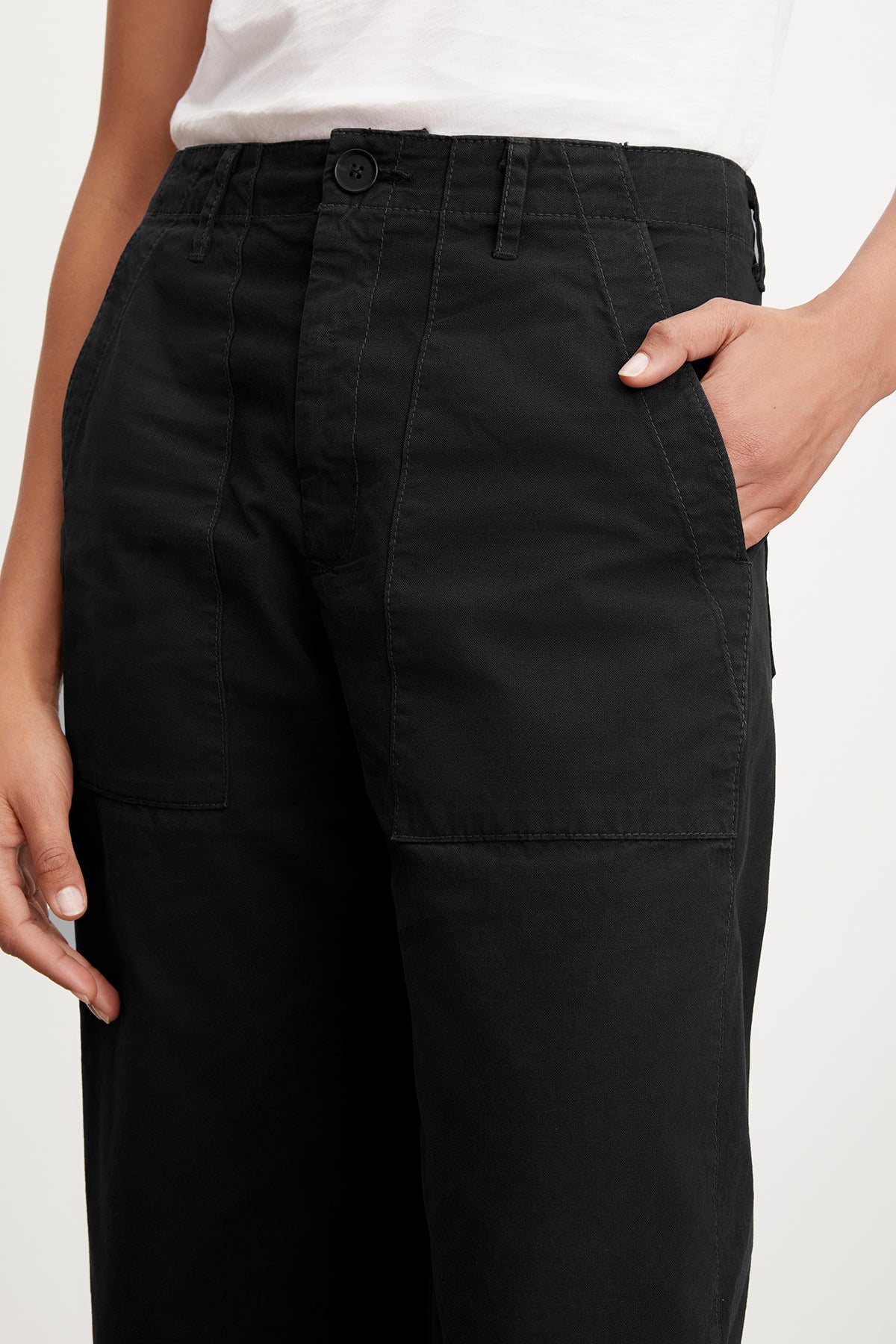 A person wearing black MYA COTTON CANVAS PANT by Velvet by Graham & Spencer with hands partially in pockets, displaying the front and waist area clearly.-36409563414721