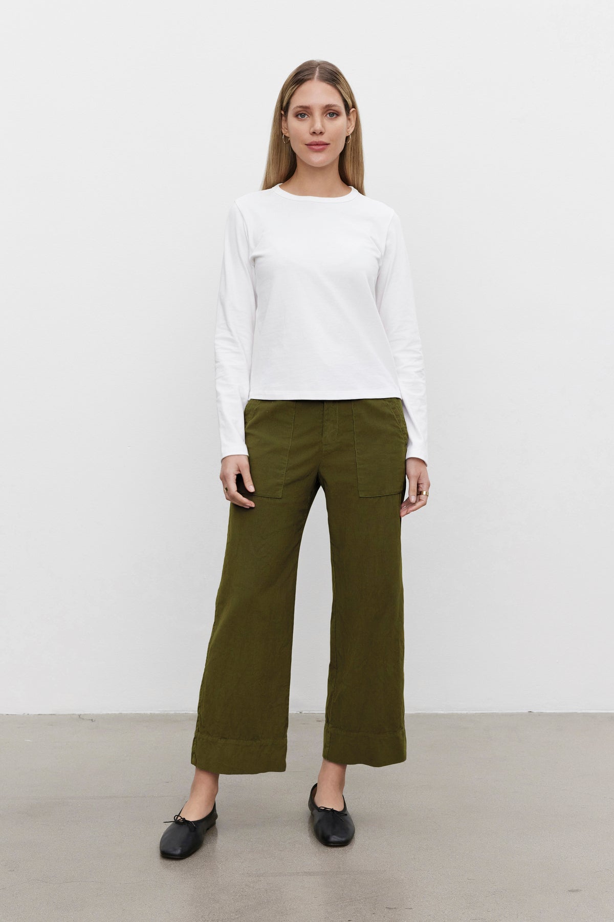 A person stands against a plain white background wearing a white long-sleeve shirt, the VERA CORDUROY PANT by Velvet by Graham & Spencer in olive green, and black shoes.-37817501253825