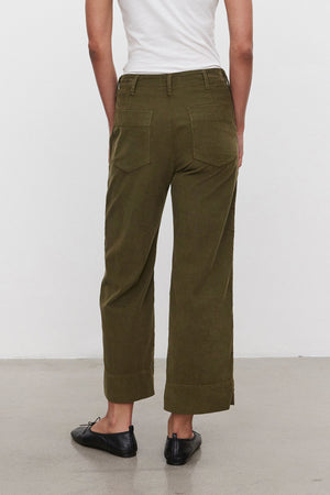 A person stands with their back to the camera, donning a white top, VERA CORDUROY PANT by Velvet by Graham & Spencer—olive green pinwale corduroy wide-leg pants featuring utility details and pockets—and black flats.