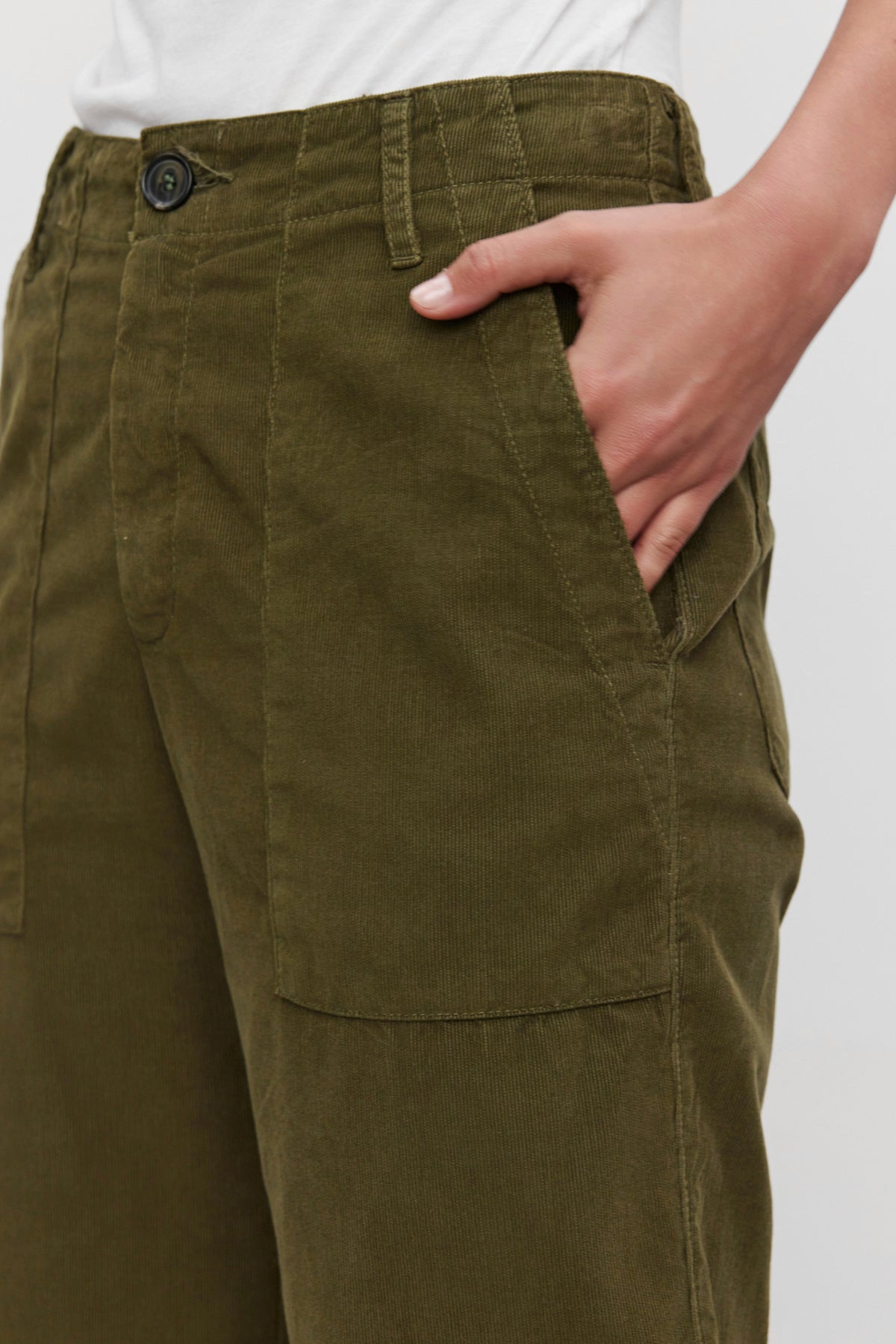 Close-up of a person wearing the VERA CORDUROY PANT from Velvet by Graham & Spencer in green, featuring pinwale corduroy fabric and cropped wide legs, with one hand in the pocket and a white shirt partially visible at the top.-37676951470273