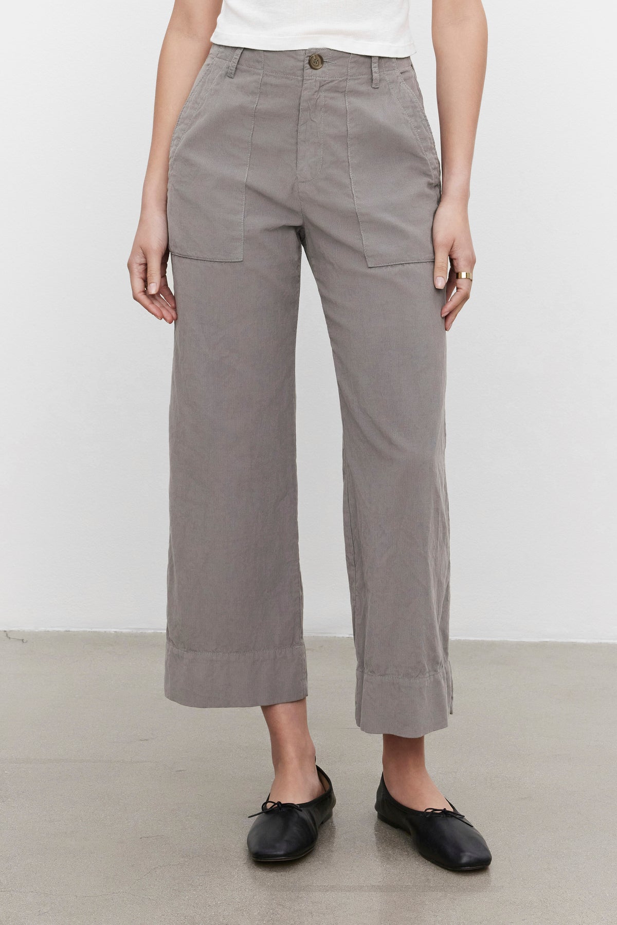   A person is wearing the flattering silhouette VERA CORDUROY PANT in gray by Velvet by Graham & Spencer, paired with a white top and black shoes. The photo is taken indoors against a plain background. 