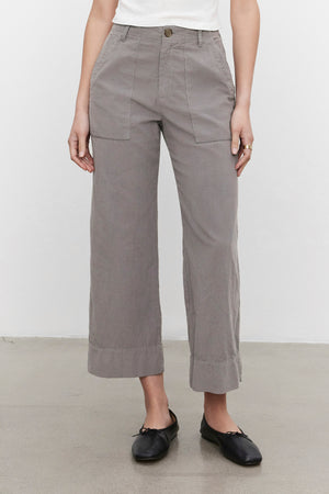 A person is wearing the flattering silhouette VERA CORDUROY PANT in gray by Velvet by Graham & Spencer, paired with a white top and black shoes. The photo is taken indoors against a plain background.