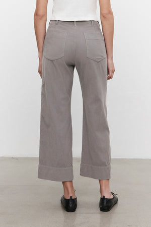 A person stands with their back to the camera, donning the VERA CORDUROY PANT in light gray by Velvet by Graham & Spencer, which creates a flattering silhouette. They pair it with black shoes against a plain background.