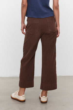 A person wearing a blue shirt and the VERA CORDUROY PANT by Velvet by Graham & Spencer is standing on a gray floor facing away from the camera.