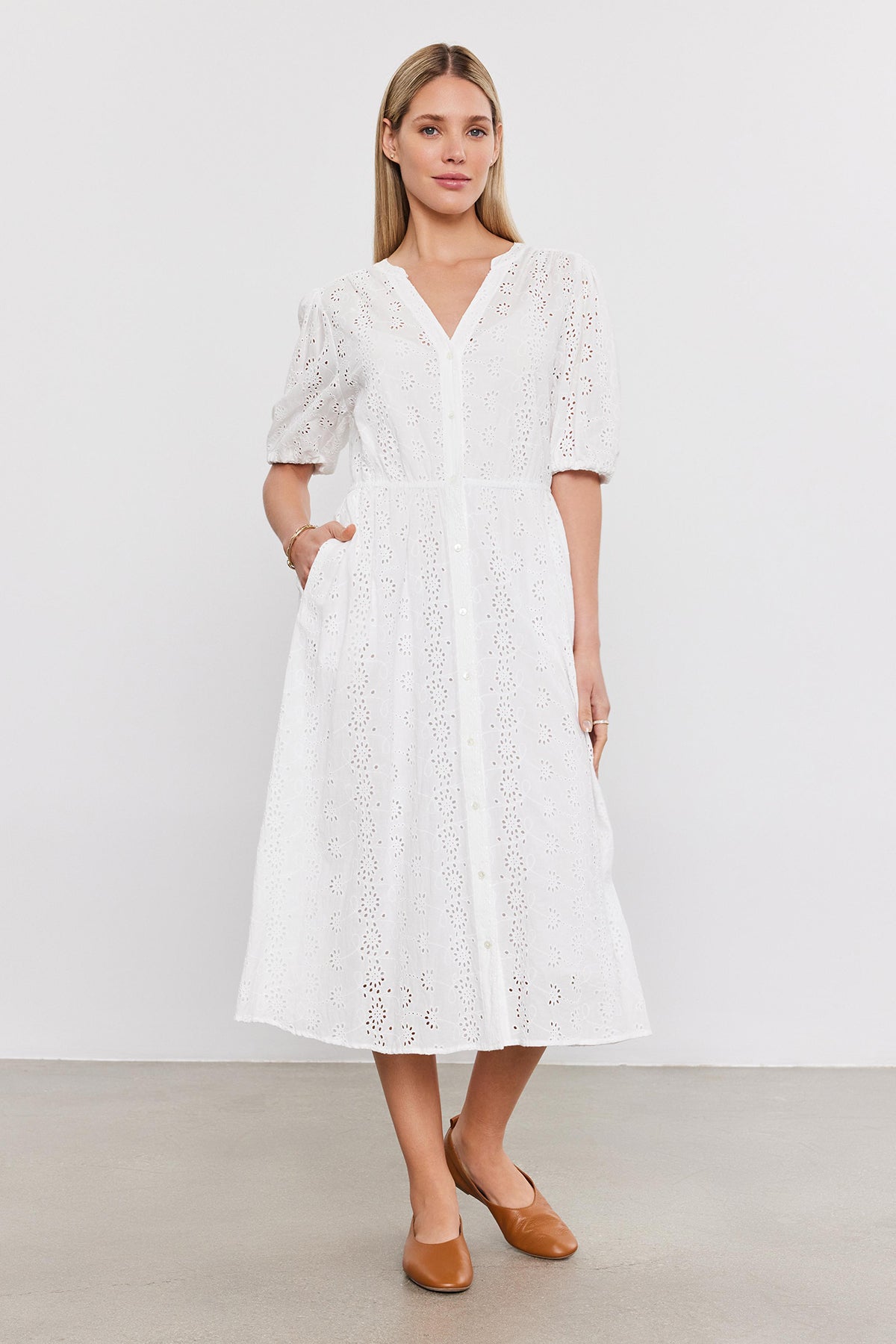 A woman stands in a studio wearing a white cotton eyelet midi dress with puff sleeves, paired with brown leather flats - the Velvet by Graham & Spencer RORI DRESS.-36910267924673