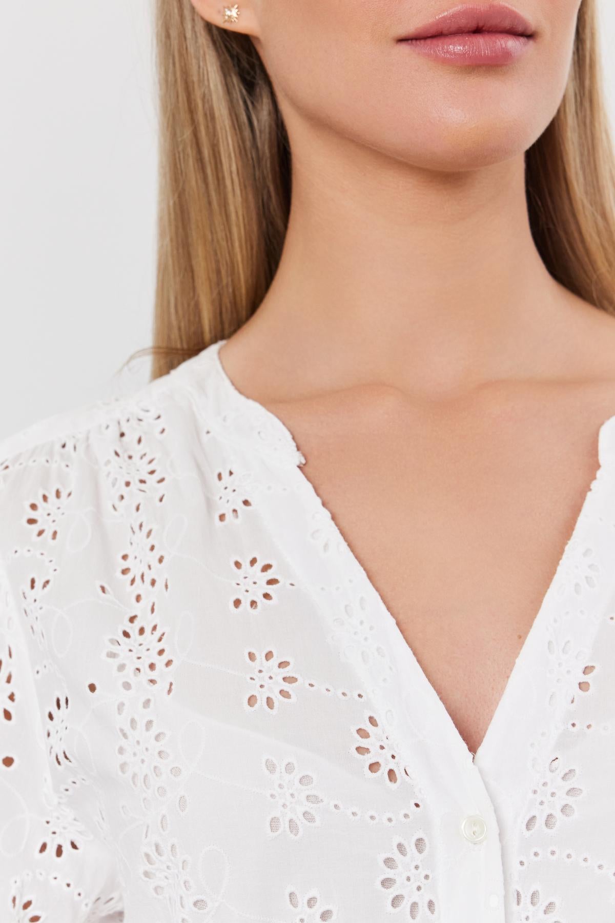   Close-up of a woman wearing a white cotton eyelet RORI DRESS by Velvet by Graham & Spencer with puff sleeves, focusing on the detailed fabric pattern and a small earring. 