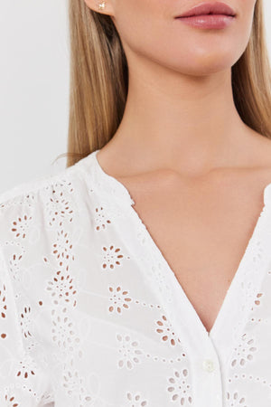Close-up of a woman wearing a white cotton eyelet RORI DRESS by Velvet by Graham & Spencer with puff sleeves, focusing on the detailed fabric pattern and a small earring.