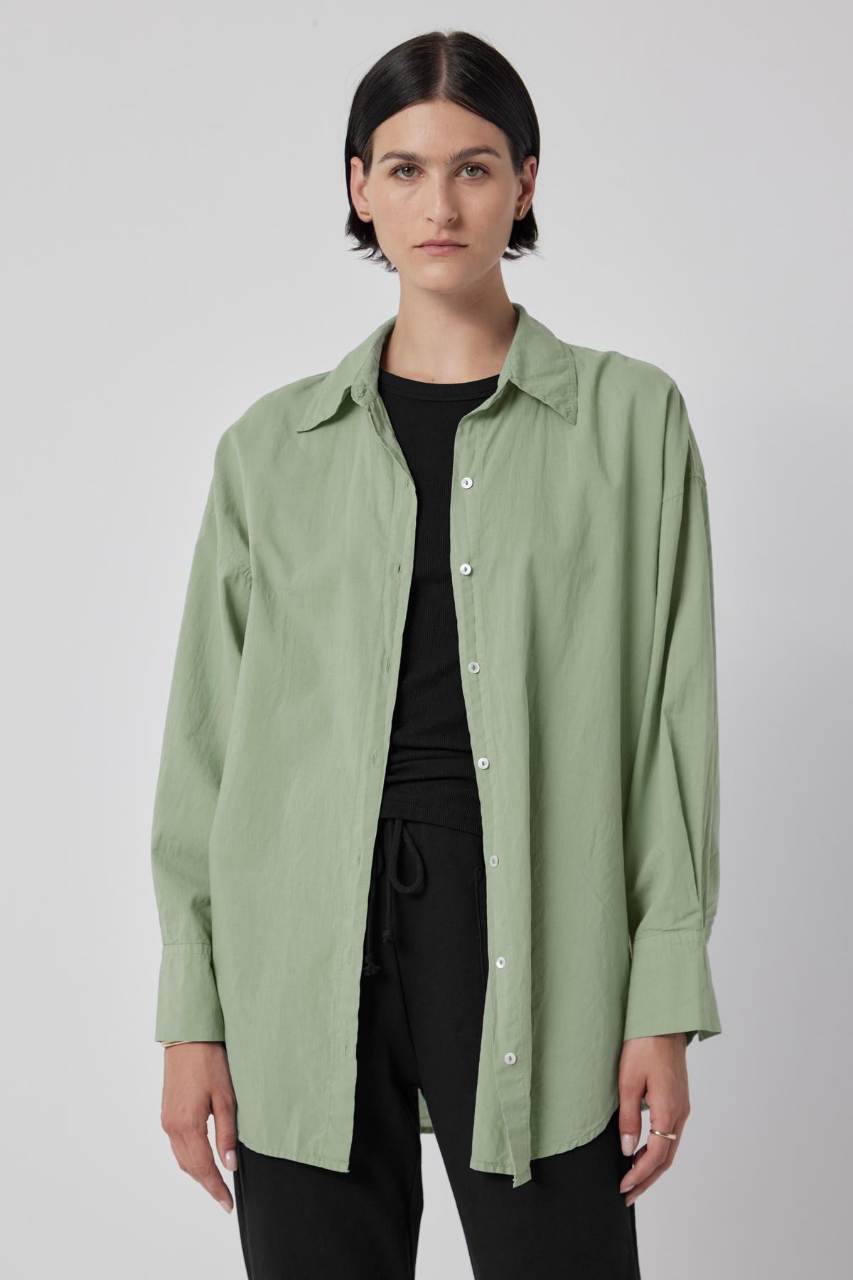   A woman wearing an oversized green REDONDO BUTTON-UP SHIRT by Velvet by Jenny Graham and black pants. 