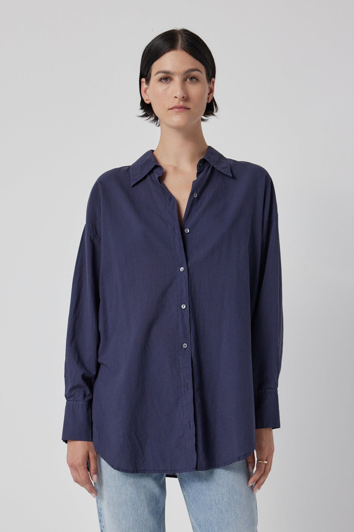   Woman wearing an oversized navy blue REDONDO BUTTON-UP SHIRT by Velvet by Jenny Graham and light blue jeans against a white background. 