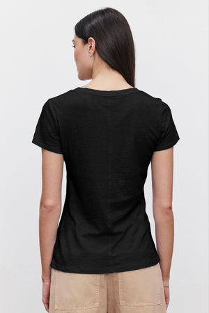 A person with long, dark hair wearing a luxurious LILITH TEE by Velvet by Graham & Spencer and beige pants is standing with their back to the camera.