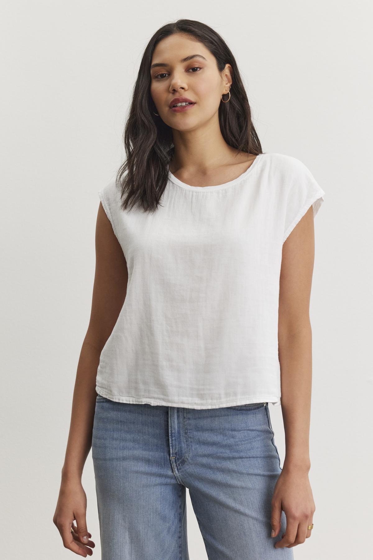   A woman with dark hair, wearing the DANIELLA CREW NECK TEE by Velvet by Graham & Spencer and blue jeans, stands against a plain white background. 
