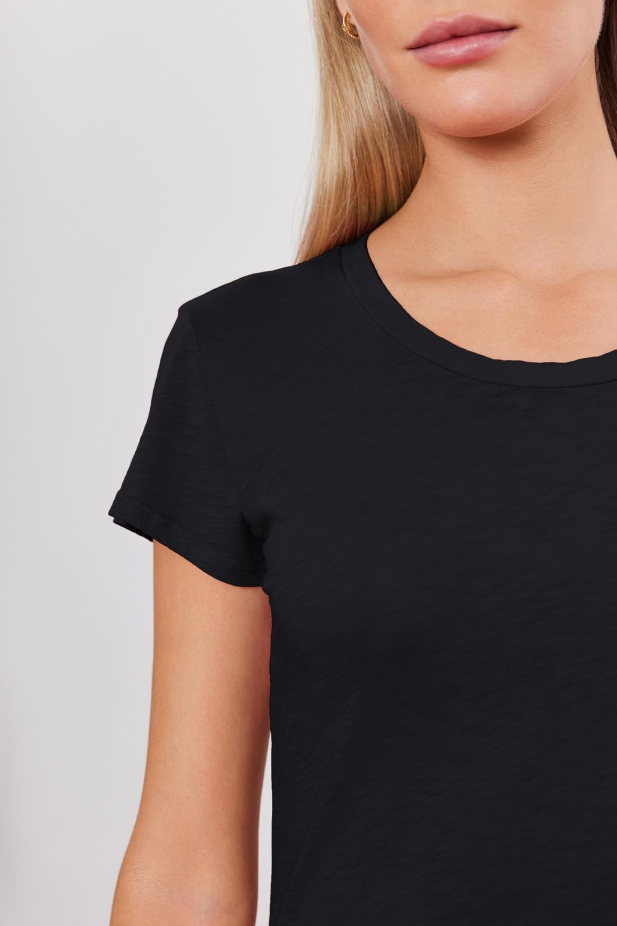 Person wearing a Velvet by Graham & Spencer ODELIA TEE, a plain black short-sleeved t-shirt made of premium cotton slub, visible from shoulders to mid-torso.-36273858609345