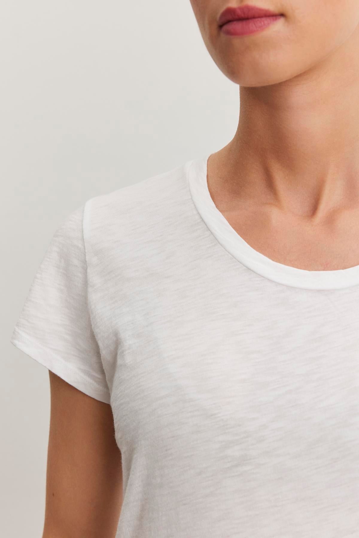   Close-up of a person wearing the ODELIA TEE by Velvet by Graham & Spencer with a round neckline. Crafted from premium cotton slub fabric, the shirt's versatility makes it a true wardrobe essential. The person's head is slightly turned, showing part of their face and neck. 