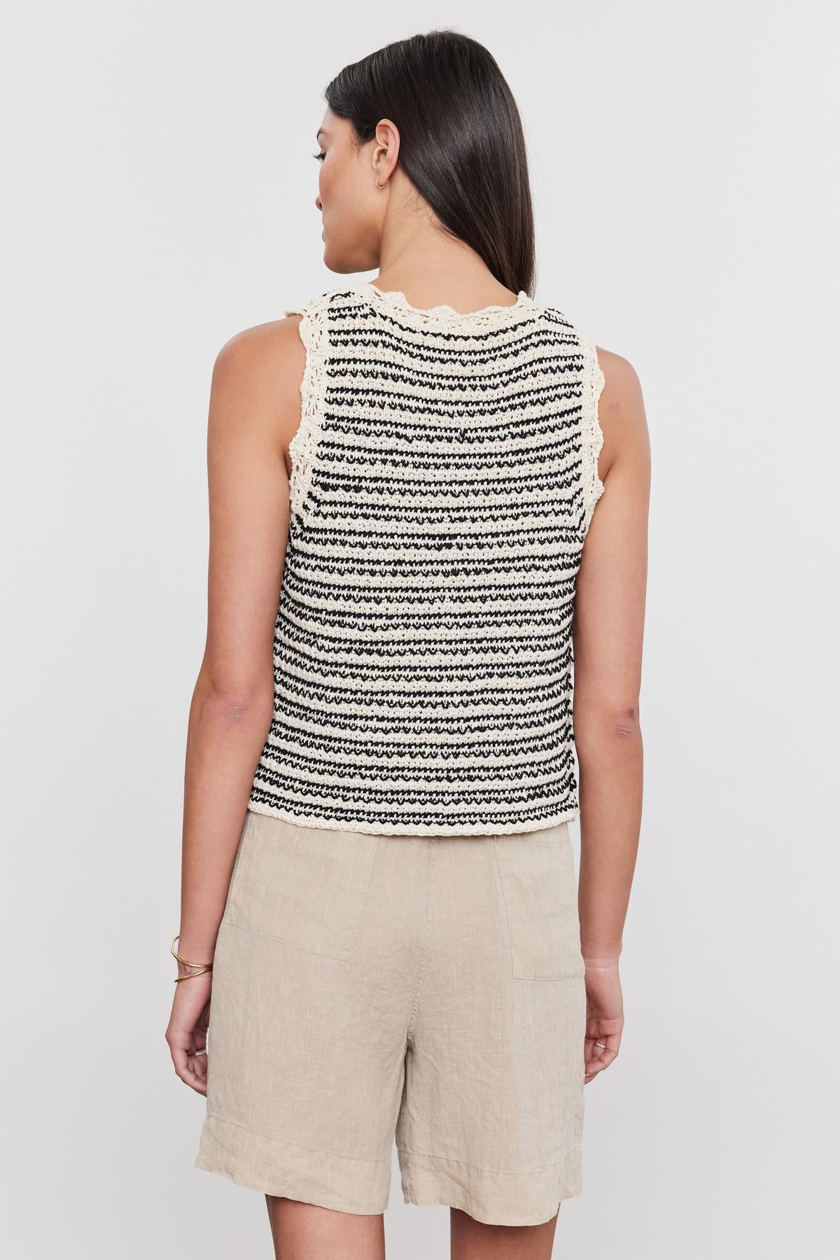   Woman standing with her back to the camera, wearing a black and white striped SOPHIE SWEATER VEST sleeveless top with a crew neckline and beige shorts by Velvet by Graham & Spencer. 