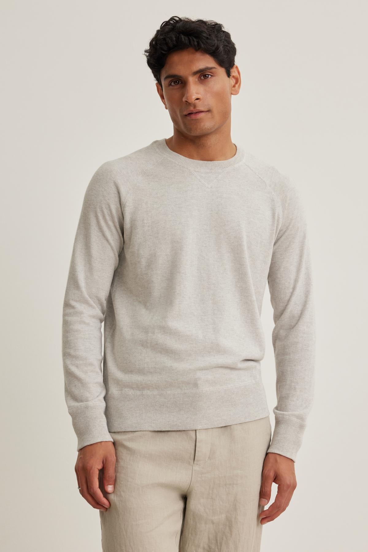 A person stands against an off-white background, wearing the DARIO COTTON CASHMERE SWEATER by Velvet by Graham & Spencer and beige pants, looking at the camera.-38643252822209