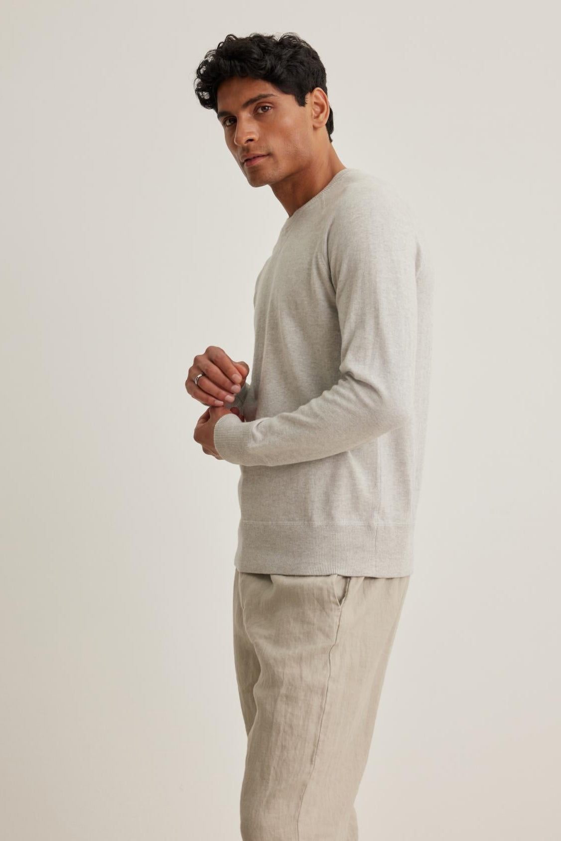   A person wearing the DARIO COTTON CASHMERE SWEATER by Velvet by Graham & Spencer in light gray, paired with beige pants, stands in a side view against a plain white background. 